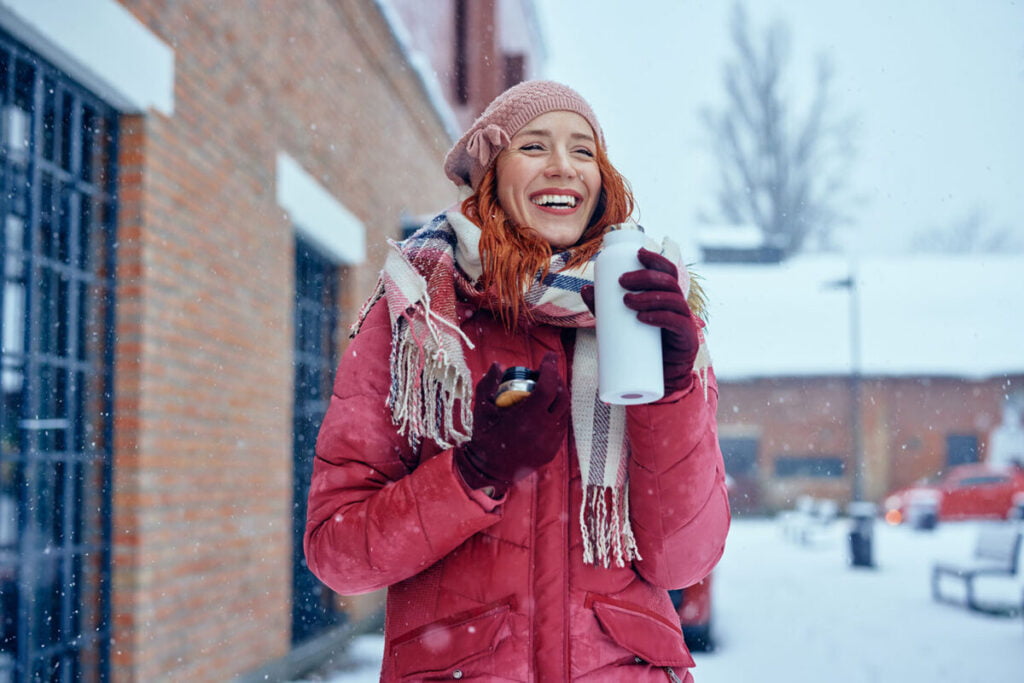 woman with a beverage bottle in her hands, smiling while it snows