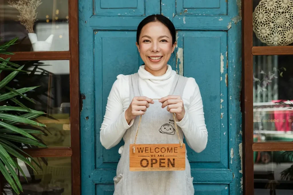 Woman holding Open sign in front of her New York City based store